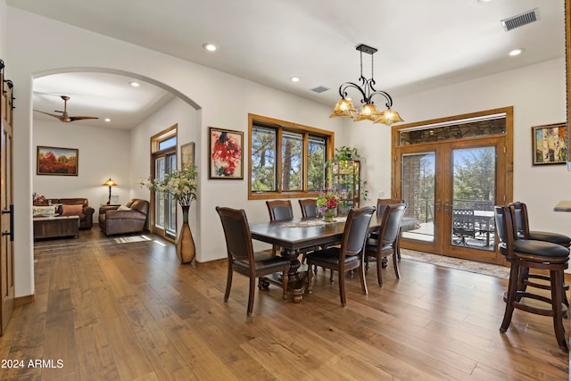 dining room with french doors, a wealth of natural light, hardwood / wood-style floors, and ceiling fan with notable chandelier