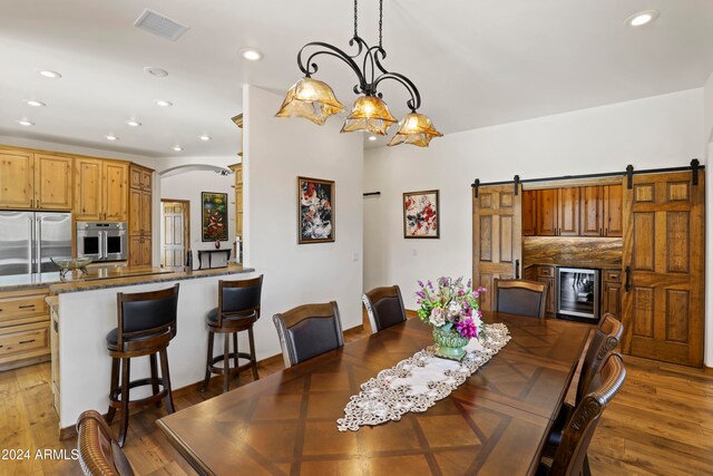 dining room with a chandelier, wood-type flooring, a barn door, and beverage cooler