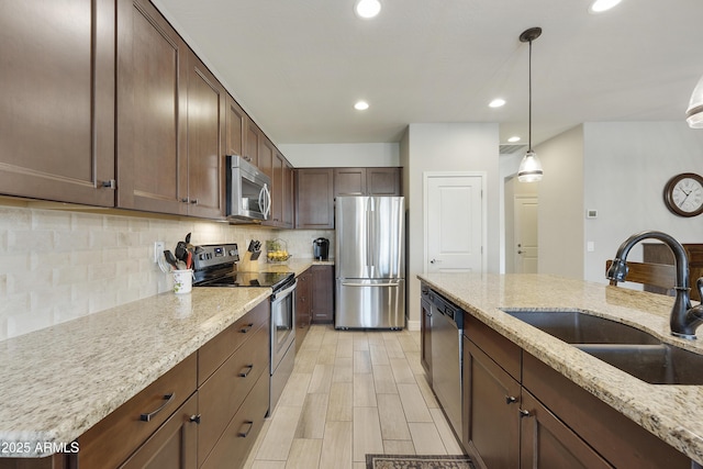 kitchen featuring light stone counters, stainless steel appliances, sink, and hanging light fixtures