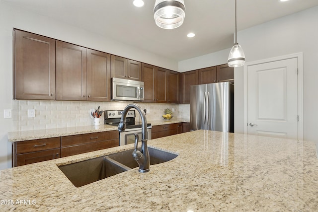 kitchen with dark brown cabinetry, light stone counters, decorative light fixtures, appliances with stainless steel finishes, and decorative backsplash