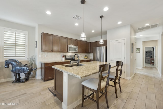 kitchen with sink, a kitchen bar, hanging light fixtures, stainless steel appliances, and light stone countertops