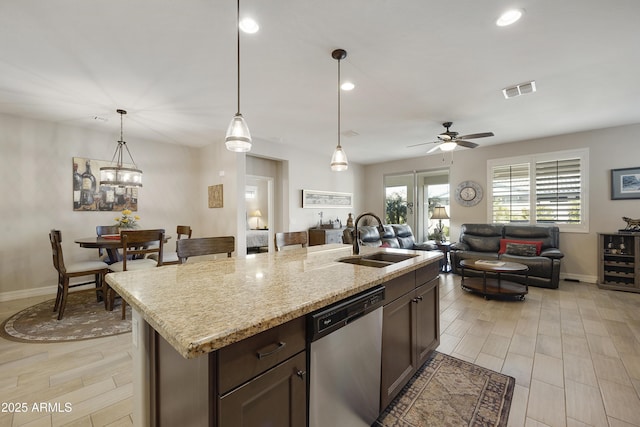 kitchen with stainless steel dishwasher, an island with sink, light stone countertops, and sink