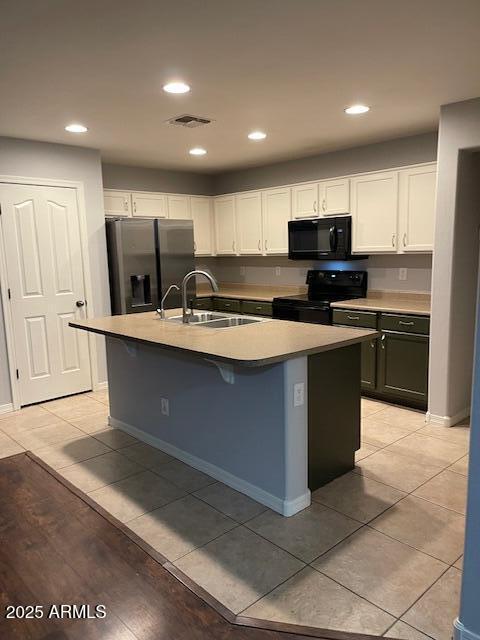 kitchen with sink, white cabinetry, a center island with sink, black appliances, and light tile patterned flooring