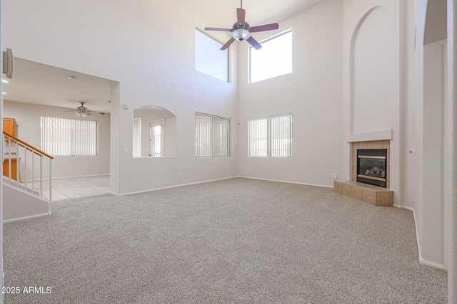 unfurnished living room featuring a tiled fireplace, light carpet, a towering ceiling, and ceiling fan