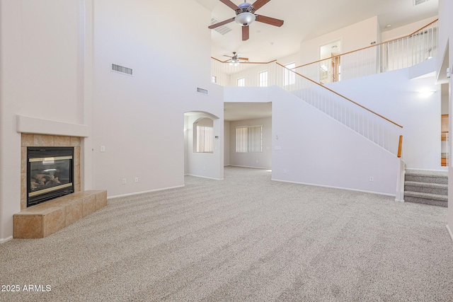 unfurnished living room with a tile fireplace, ceiling fan, carpet floors, and a high ceiling