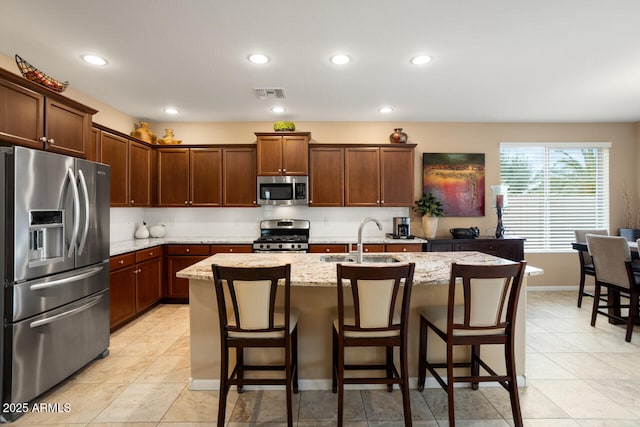 kitchen featuring visible vents, a sink, stainless steel appliances, decorative backsplash, and light stone countertops