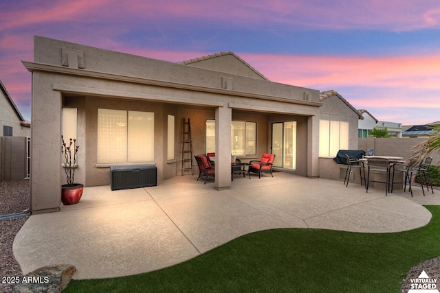 back of property at dusk with a patio area, stucco siding, and fence