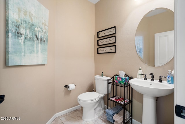 half bathroom with tile patterned floors, baseboards, toilet, and a sink