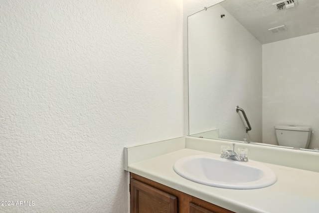 bathroom with a textured ceiling, vanity, and toilet