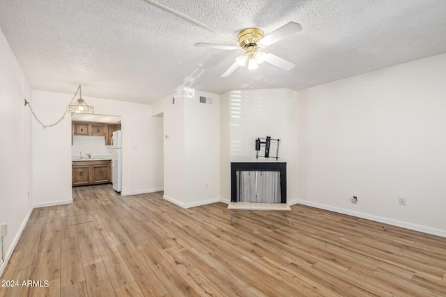 unfurnished living room with a textured ceiling, sink, ceiling fan, and light wood-type flooring