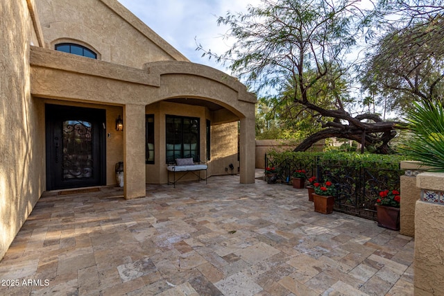 doorway to property featuring stucco siding, fence, and a patio