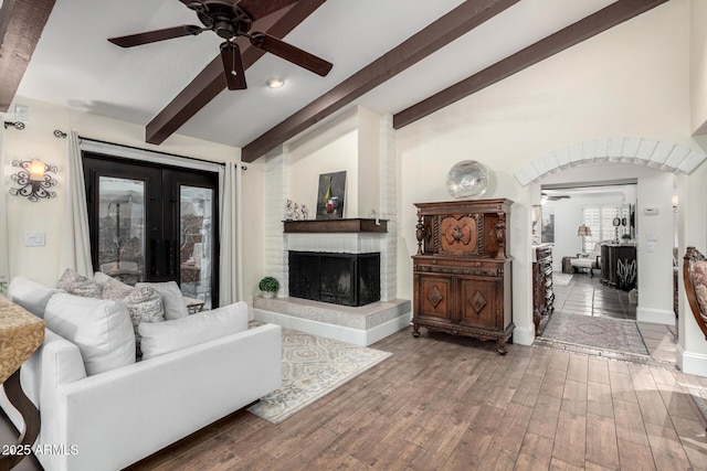 living room with arched walkways, lofted ceiling with beams, a large fireplace, wood finished floors, and french doors