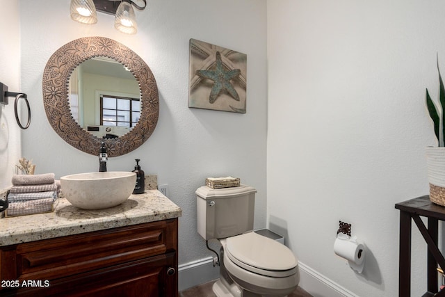 half bathroom with baseboards, vanity, and toilet