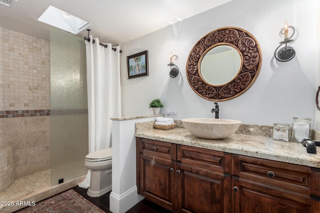 full bathroom with a skylight, tiled shower, vanity, and toilet