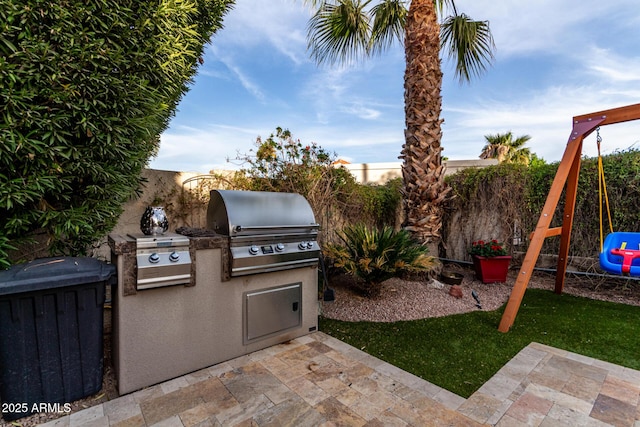 view of patio / terrace with exterior kitchen, a fenced backyard, a playground, and area for grilling