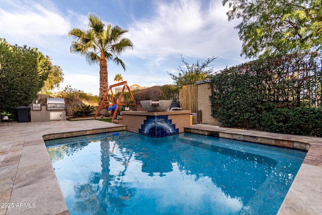 view of swimming pool with a patio, grilling area, fence, exterior kitchen, and a playground