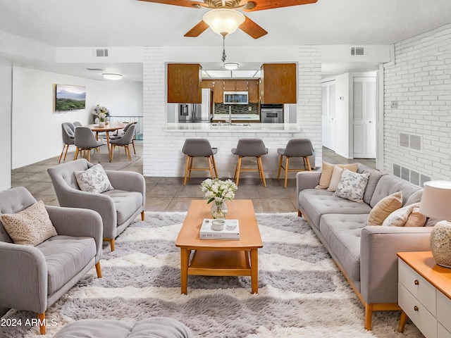 living room with light tile patterned floors, ceiling fan, and brick wall