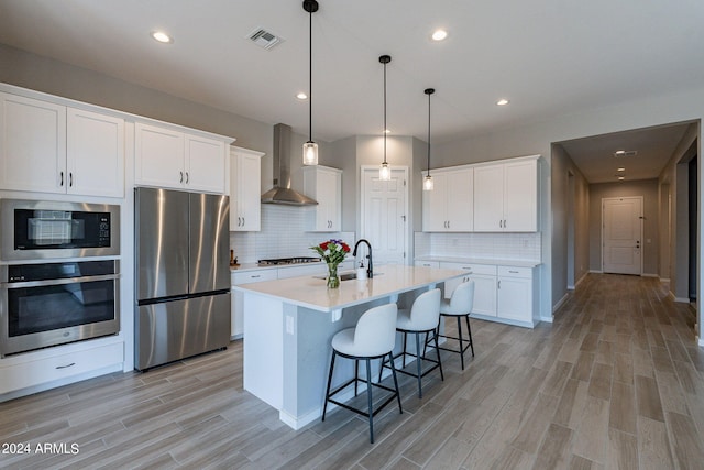 kitchen featuring light hardwood / wood-style flooring, stainless steel appliances, sink, wall chimney range hood, and white cabinets