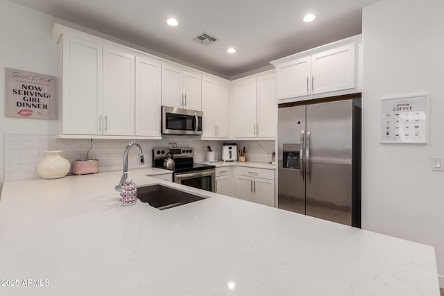 kitchen with appliances with stainless steel finishes, a sink, tasteful backsplash, white cabinets, and recessed lighting