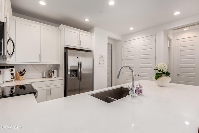 kitchen featuring stainless steel appliances, a sink, recessed lighting, decorative backsplash, and white cabinetry