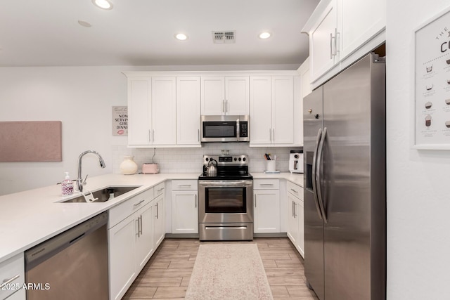 kitchen featuring stainless steel appliances, a sink, white cabinetry, tasteful backsplash, and light wood finished floors