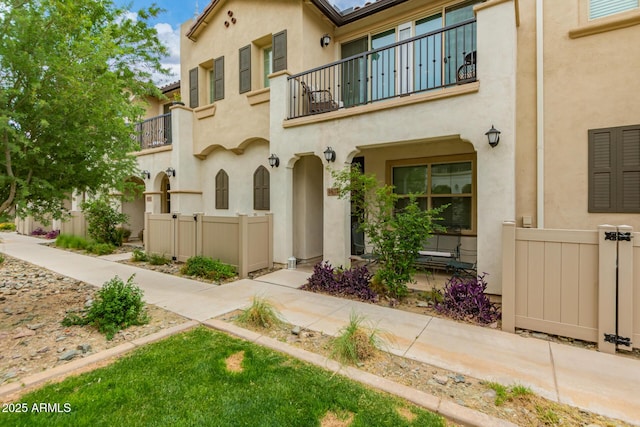 view of front of property featuring a balcony, stucco siding, and fence