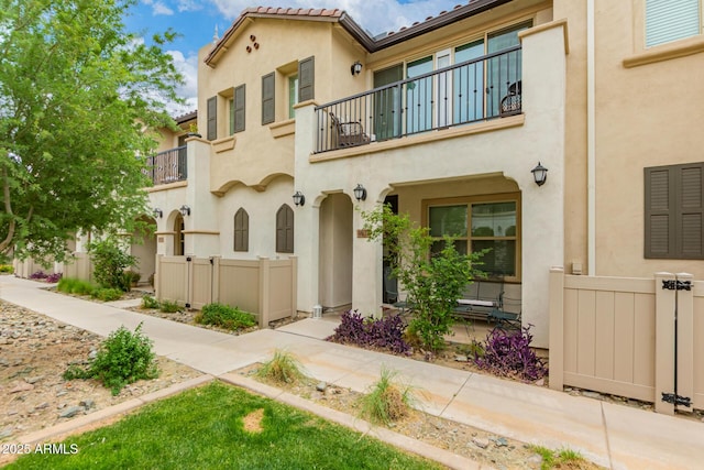 view of front of house with a balcony, stucco siding, and fence