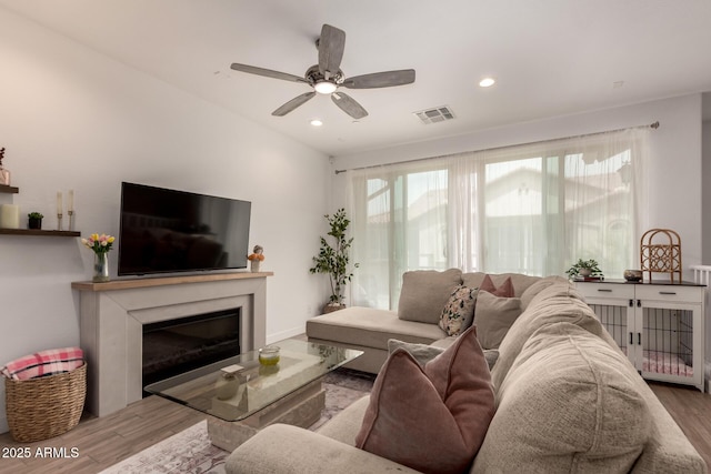 living room featuring wood finished floors, a glass covered fireplace, ceiling fan, and recessed lighting