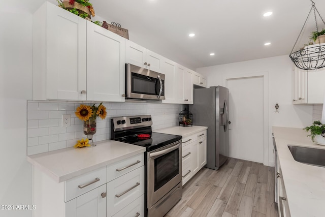 kitchen with white cabinetry, sink, stainless steel appliances, light hardwood / wood-style floors, and decorative backsplash