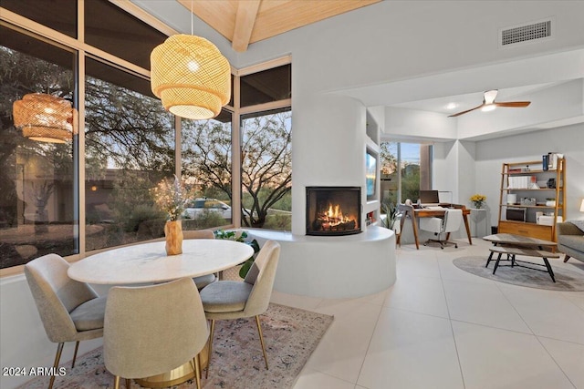 tiled dining area with ceiling fan, beamed ceiling, and a fireplace