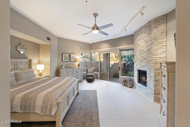 bedroom with ceiling fan, access to outside, a stone fireplace, track lighting, and light tile patterned flooring