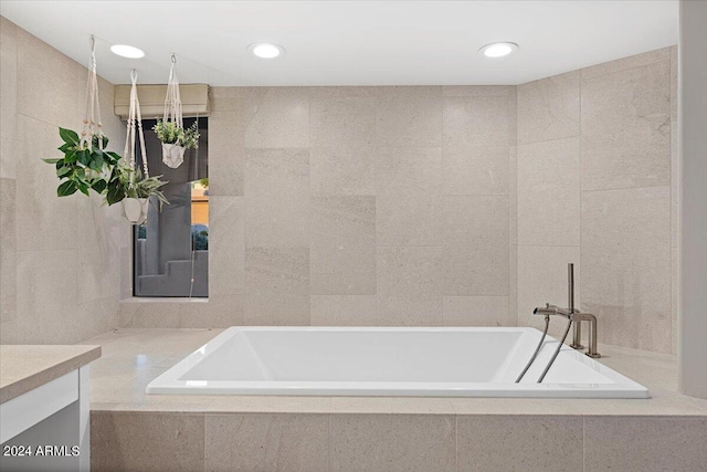 bathroom with tiled bath, tile walls, and vanity