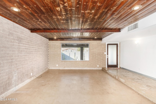 spare room featuring beamed ceiling, concrete floors, wooden ceiling, and brick wall