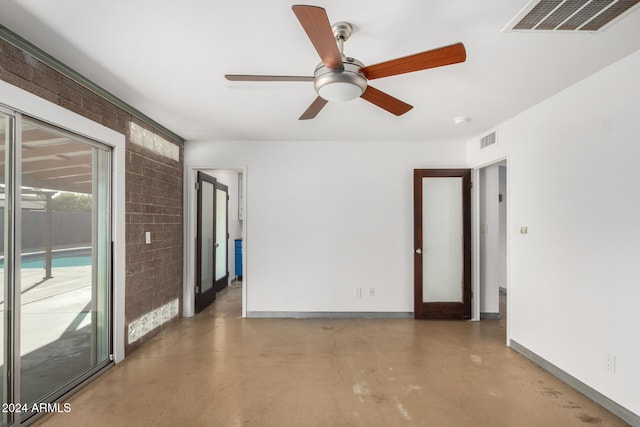 empty room featuring concrete flooring, ceiling fan, and brick wall