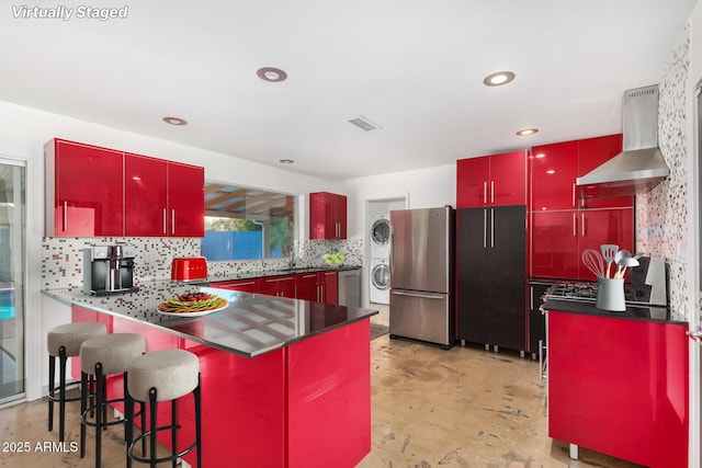 3033 E Sierra St, Phoenix, AZ 85028 - kitchen with red cabinetry, wall chimney exhaust hood, stainless steel appliances, stacked washer / dryer, and concrete floors
