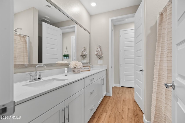 full bath with a sink, baseboards, double vanity, and wood finished floors