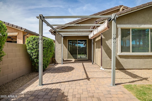 view of exterior entry featuring a patio area, stucco siding, and fence