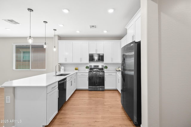 kitchen featuring appliances with stainless steel finishes, a sink, light wood-style flooring, a peninsula, and visible vents
