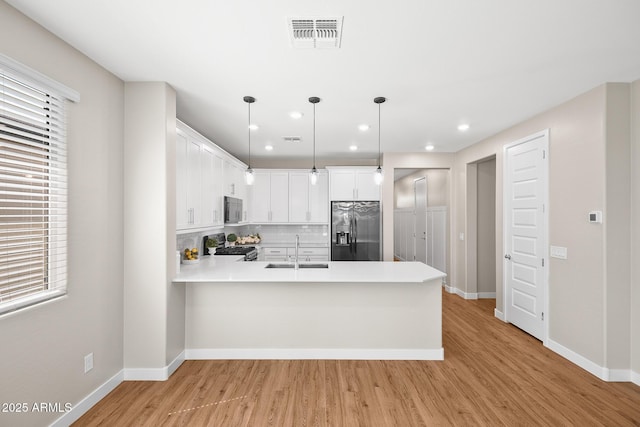 kitchen with visible vents, a sink, a peninsula, light wood-style floors, and stainless steel appliances