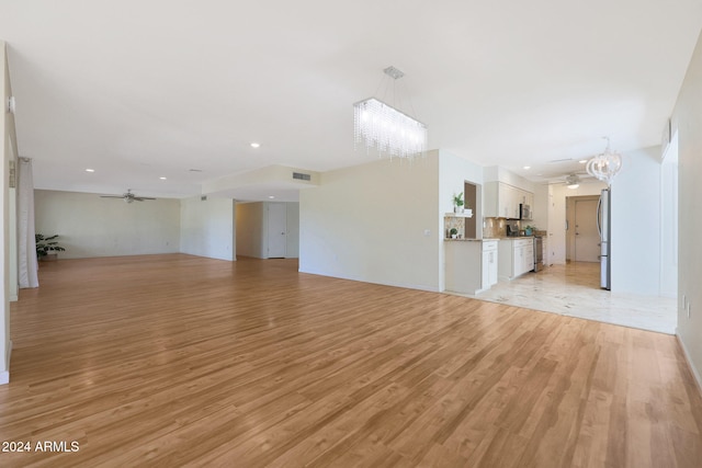 unfurnished living room with ceiling fan with notable chandelier, light wood-style flooring, visible vents, and recessed lighting