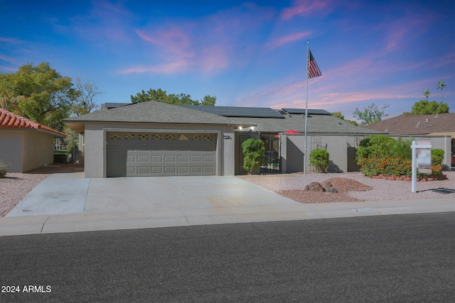 single story home featuring a garage, driveway, solar panels, and stucco siding