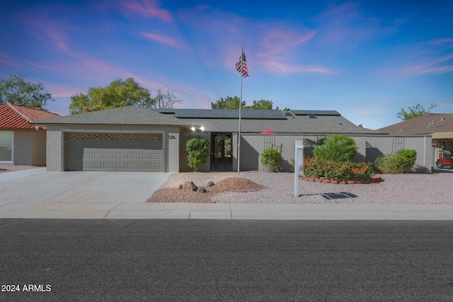 view of front facade featuring a garage, driveway, stucco siding, and roof mounted solar panels