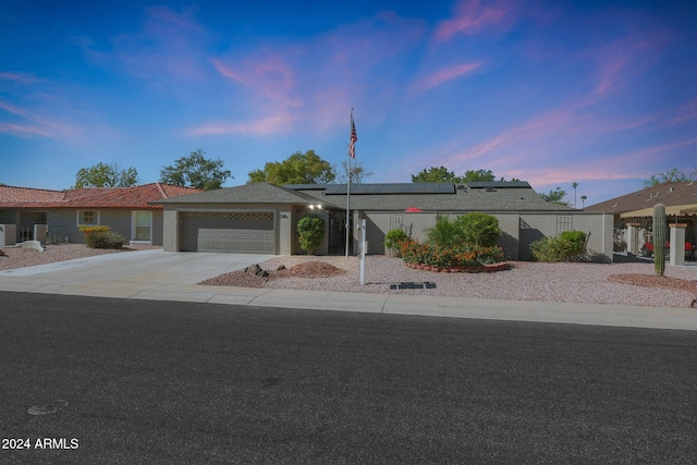 view of front of house with concrete driveway, an attached garage, fence, and roof mounted solar panels