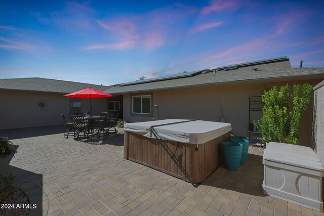 rear view of property with a hot tub, outdoor dining area, a patio area, roof mounted solar panels, and stucco siding