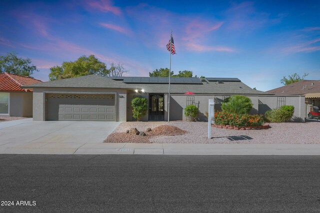 view of front of home featuring stucco siding, driveway, an attached garage, and solar panels