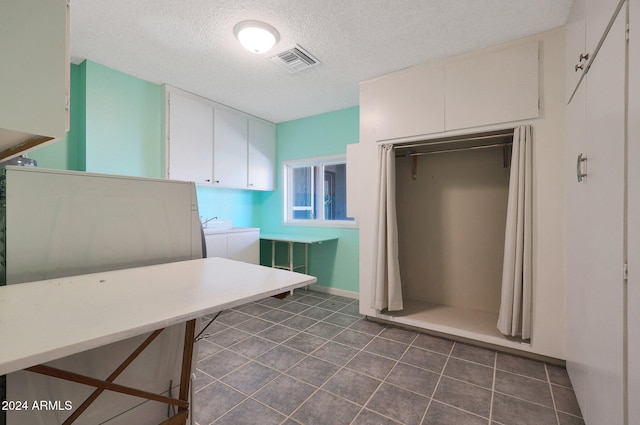 interior space featuring washing machine and clothes dryer, visible vents, a textured ceiling, dark tile patterned flooring, and laundry area