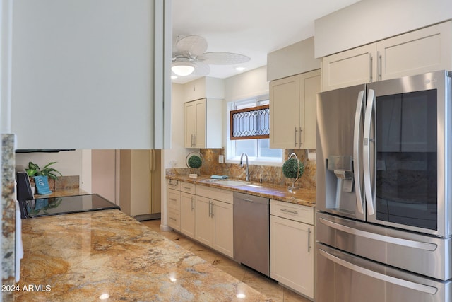 kitchen featuring ceiling fan, light stone counters, a sink, appliances with stainless steel finishes, and backsplash