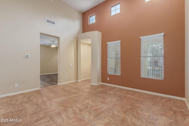 unfurnished room with visible vents, baseboards, a towering ceiling, and a ceiling fan