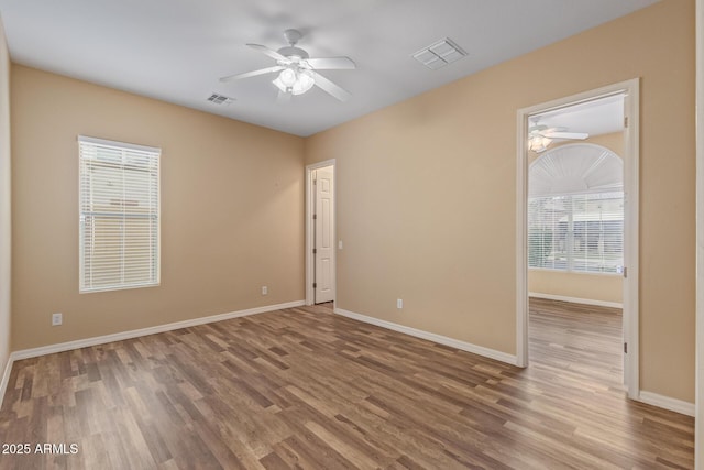 unfurnished room featuring baseboards, wood finished floors, visible vents, and ceiling fan