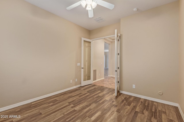 unfurnished room featuring baseboards, wood finished floors, visible vents, and ceiling fan